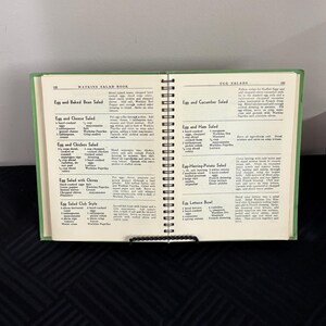 May include: A vintage Watkins Salad Book with recipes for egg salads. The book is open to a page with recipes for Egg and Baked Bean Salad, Egg and Cheese Salad, Egg and Chicken Salad, Egg Salad with Chives, Egg Salad Club Style, Egg and Cucumber Salad, Egg and Ham Salad, Egg-Herring-Potato Salad, and Egg Lettuce Bowl.