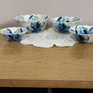 Puede incluir: Conjunto de cuatro cuencos de cer&aacute;mica blanca con bordes festoneados. Cada cuenco presenta un dise&ntilde;o floral azul pintado a mano con detalles verdes. Los cuencos est&aacute;n colocados sobre un tapete de encaje blanco.