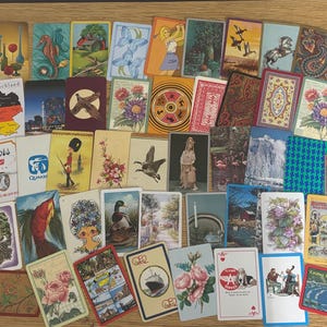 May include: A large collection of rectangular vintage postcards and playing cards featuring diverse illustrations including landscapes, animals, flowers, ships, and various graphic designs arranged in a scattered overlapping layout.
