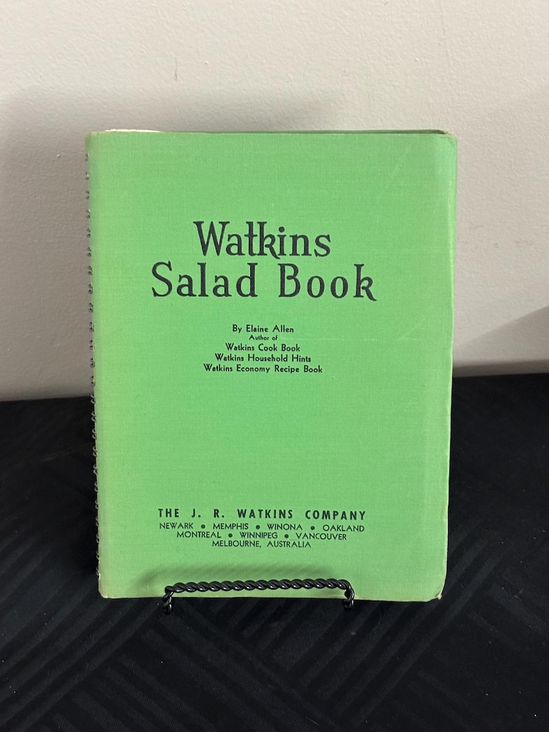 May include: A green book titled "Watkins Salad Book" by Elaine Allen. The book is a collection of recipes for salads, as well as other Watkins products. The book was published by The J. R. Watkins Company, which is located in Newark, Memphis, Winona, Oakland, Montreal, Winnipeg, Vancouver, and Melbourne, Australia.