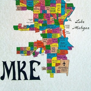May include: A colorful map of Milwaukee, Wisconsin, with the city's neighborhoods labeled in different colors. The map is surrounded by a black border and includes a compass rose in the top right corner. The text "MKE" is written in large, black letters at the bottom of the map.