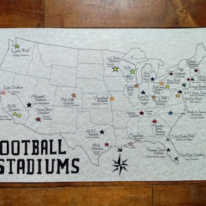 May include: A black and white map of the United States with a compass rose in the bottom right corner. The map shows the locations of various football stadiums across the country. Each stadium is marked with a star in a different color. The text "FOOTBALL STADIUMS" is written in large, bold letters at the bottom of the map.
