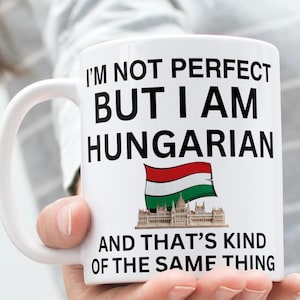 May include: White ceramic mug with the text "I'M NOT PERFECT BUT I AM HUNGARIAN" in black. The mug features the Hungarian flag and a depiction of the Hungarian Parliament Building. The phrase "AND THAT'S KIND OF THE SAME THING" is printed below.