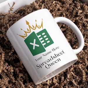 May include: White ceramic mug with a green and white Excel logo and a gold crown. The text "Your Name Here - Spreadsheet Queen" is printed on the mug.