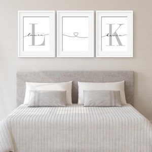May include: Three white framed prints with grey lettering. The left print has the letter "L" with the name "Laura" written in cursive above it. The middle print has a heart symbol with a line extending to the left and right. The right print has the letter "K" with the name "Kevin" written in cursive above it.