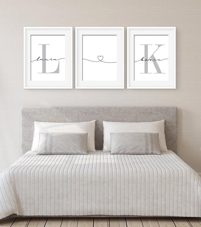 May include: Three white framed prints with grey lettering. The left print has the letter "L" with the name "Laura" written in cursive above it. The middle print has a heart symbol with a line extending to the left and right. The right print has the letter "K" with the name "Kevin" written in cursive above it.