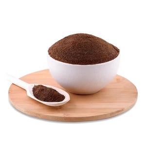 May include: A white bowl filled with dark brown ground coffee powder sits on a round wooden board. A white spoon with a small amount of coffee powder is on the board.
