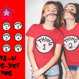 May include: Two women wearing red t-shirts with white circles that say "Thing 1" and "Thing 2" on them. The women are smiling and have their hair pulled back.