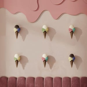 May include: A pink ice cream parlor interior with a velvet booth, round marble table, and decorative ice cream cone wall art. The wall features a pink, wavy design. The floor has a terrazzo pattern.