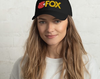 Puede incluir: Una gorra de béisbol negra con una cabeza de zorro roja y la palabra "FOX" bordada en amarillo.