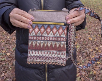 May include: A small, patterned crossbody bag with a zipper closure and a brown and beige fabric strap. The bag has a geometric design with red, blue, and yellow accents.