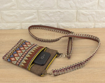 May include: A small brown and red patterned crossbody bag with a zippered pocket and a black phone inside. The bag has a long adjustable strap with a geometric pattern.