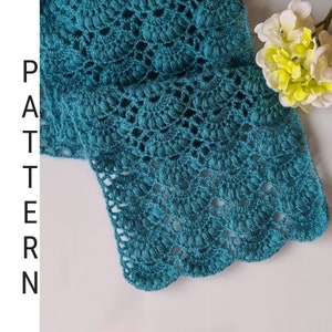 Puede incluir: Bufanda de crochet de color turquesa con un delicado patrón de encaje. La bufanda está doblada por la mitad y tiene un borde festoneado.