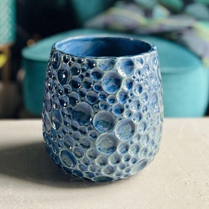 May include: A blue ceramic planter with a textured bubble design. The planter is sitting on a light grey surface.