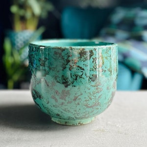 May include: A teal ceramic planter with a textured, metallic finish. The planter has a rounded shape and a wide base.