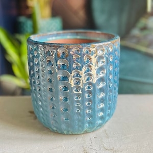 May include: A blue ceramic planter with a textured, bubble-like surface. The planter is empty and sitting on a white surface.