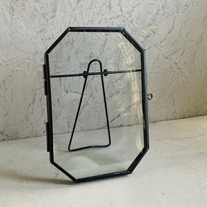 May include: A black octagonal picture frame with a glass front and a metal stand. The frame is empty.