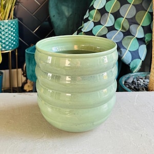 May include: A light green ceramic planter with a ribbed design. The planter is sitting on a light grey surface.