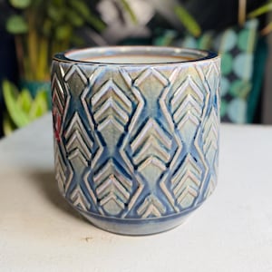 May include: A ceramic plant pot with a geometric pattern in shades of blue, grey, and white. The pot has a textured surface and a rounded base. The interior is a light cream colour.