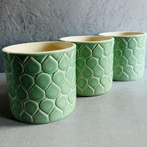 May include: Three green ceramic planters with a teardrop pattern. The planters are arranged in a row from largest to smallest.