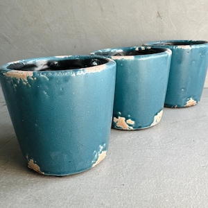 May include: Three teal blue ceramic planters with a distressed finish. The planters are arranged in a row, with the largest planter at the front and the smallest planter at the back.