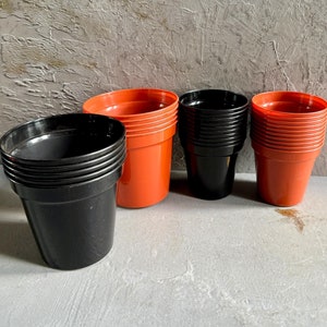 May include: A set of black and orange plastic plant pots. The pots are stacked in groups of three. The pots are on a grey textured surface.