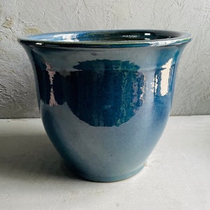 May include: A teal blue ceramic planter with a wide, rounded base and a slightly flared rim.