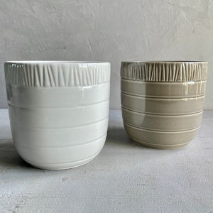 May include: Two ceramic planters, one white and one light brown, with a textured, striped design.