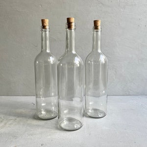 May include: Three clear glass bottles with cork stoppers. The bottles are empty and have a slightly textured surface.