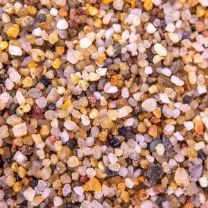 May include: A close-up view of a variety of small, colourful pebbles. The pebbles are mostly brown, white, and grey, with some red and black pebbles mixed in. The pebbles are all about the same size, and they are arranged in a random pattern.