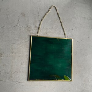 May include: A gold-colored metal picture frame with a dark green background. The frame has a chain attached to the top for hanging.