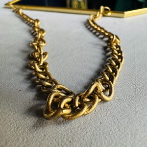 May include: A gold chain with a thick, chunky link design. The chain is hanging from a mirror, which is not visible in the image.