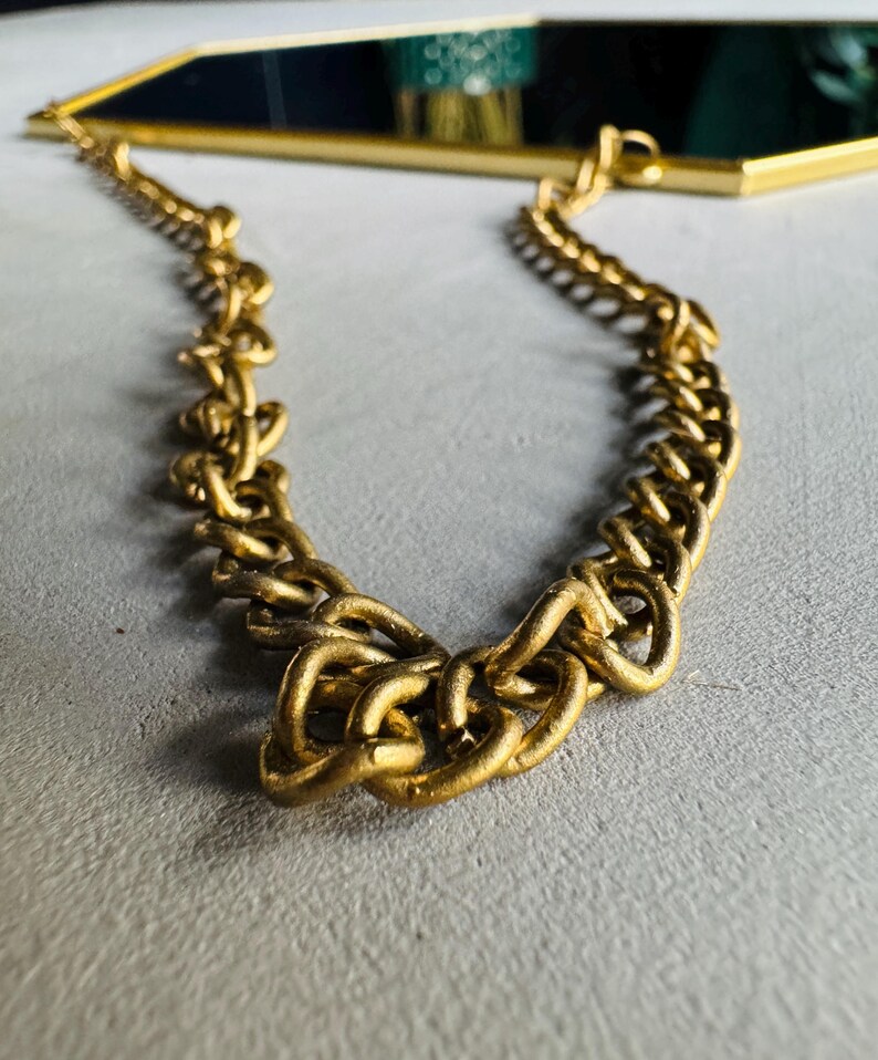 May include: A gold chain with a thick, chunky link design. The chain is hanging from a mirror, which is not visible in the image.