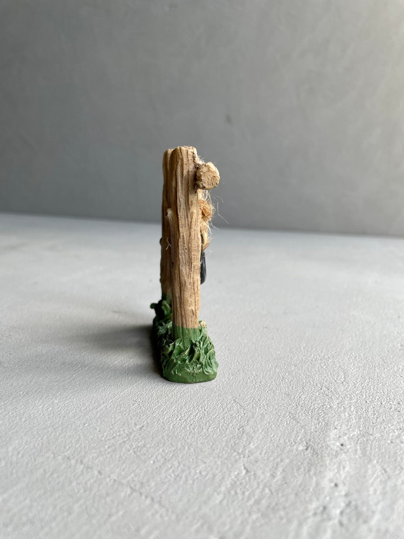 Pu&ograve; includere: Un piccolo recinto in legno in miniatura con una base verde, che presenta una piccola figura di una persona appoggiata al recinto.