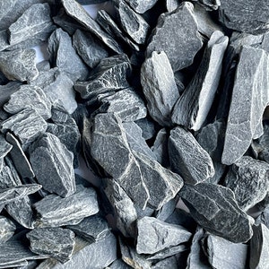 May include: A close-up view of a pile of dark grey slate chips. The chips are irregularly shaped and have a rough, textured surface.