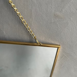 May include: A gold-framed rectangular mirror with a chain hanging from the top.