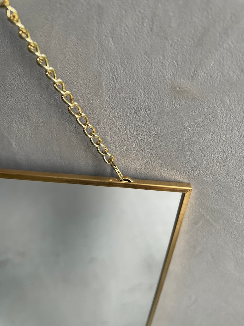 May include: A gold-framed rectangular mirror with a chain hanging from the top.
