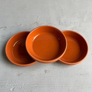 May include: Three terracotta plant saucers, each with a slightly different shade of brown. The saucers are stacked on top of each other.