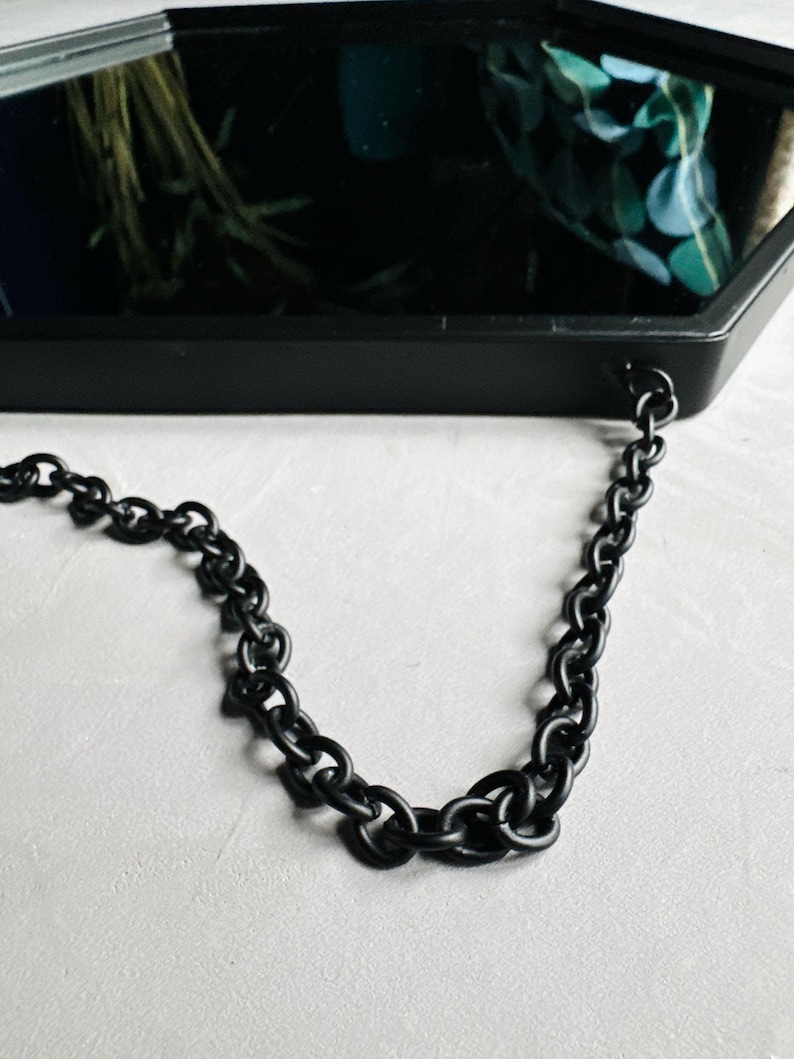 May include: A black octagonal mirror with a black chain hanging from it. The mirror is reflecting a green and blue patterned fabric.