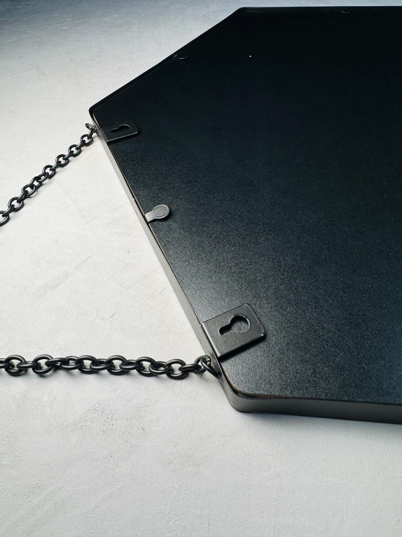 May include: Black hexagonal mirror with a chain hanging from two metal hooks on the back.