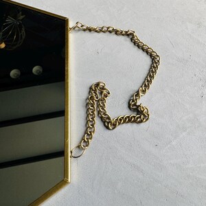 May include: A gold hexagonal mirror with a gold chain hanging from the top.