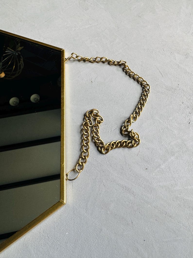 May include: A gold hexagonal mirror with a gold chain hanging from the top.
