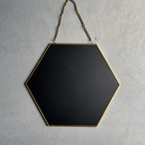 May include: A hexagonal mirror with a gold frame and a black backing. The mirror is hanging from a gold chain.
