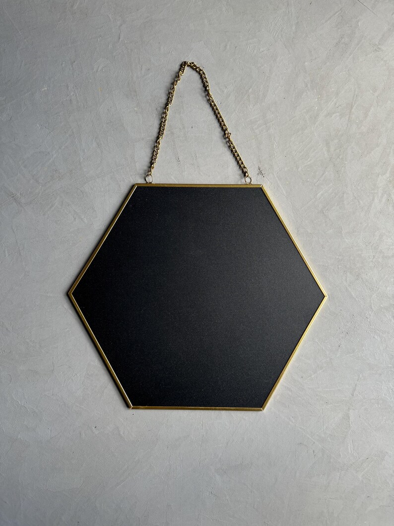 May include: A hexagonal mirror with a gold frame and a black backing. The mirror is hanging from a gold chain.