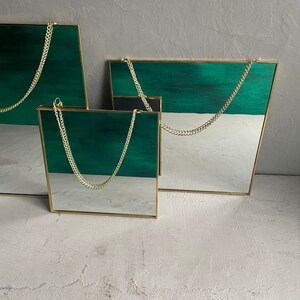 May include: Three gold framed mirrors with green and white backgrounds hanging from gold chains. The mirrors are different sizes and are arranged in a staggered pattern.