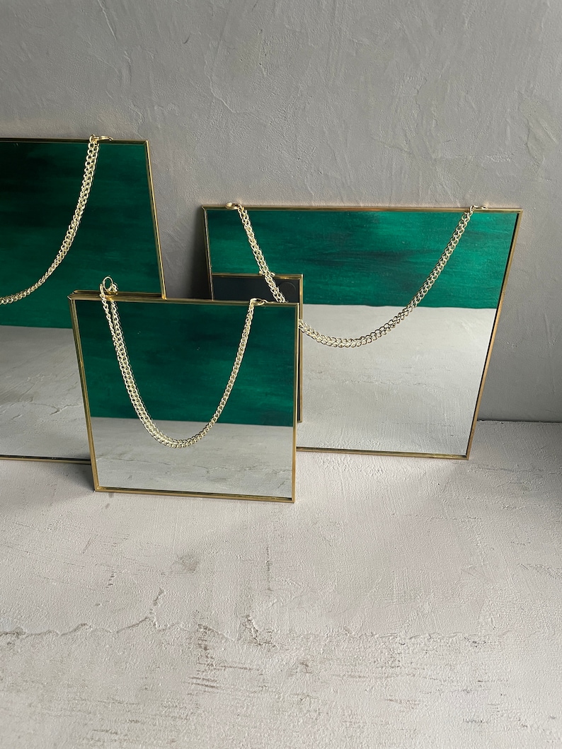 May include: Three gold framed mirrors with green and white backgrounds hanging from gold chains. The mirrors are different sizes and are arranged in a staggered pattern.