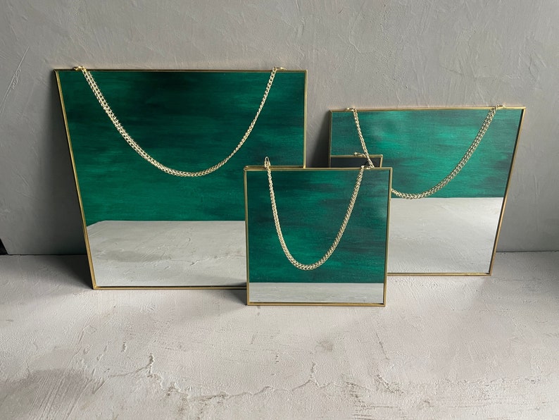 May include: Three gold framed mirrors with green glass and hanging chains. The mirrors are different sizes and are arranged in a staggered formation.