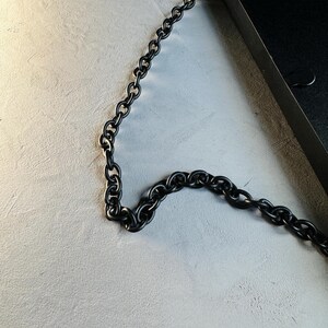 May include: A black metal chain hangs from a black metal frame. The chain is made of thick, linked rings.