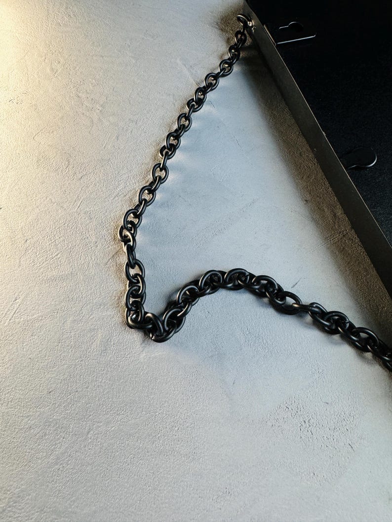 May include: A black metal chain hangs from a black metal frame. The chain is made of thick, linked rings.