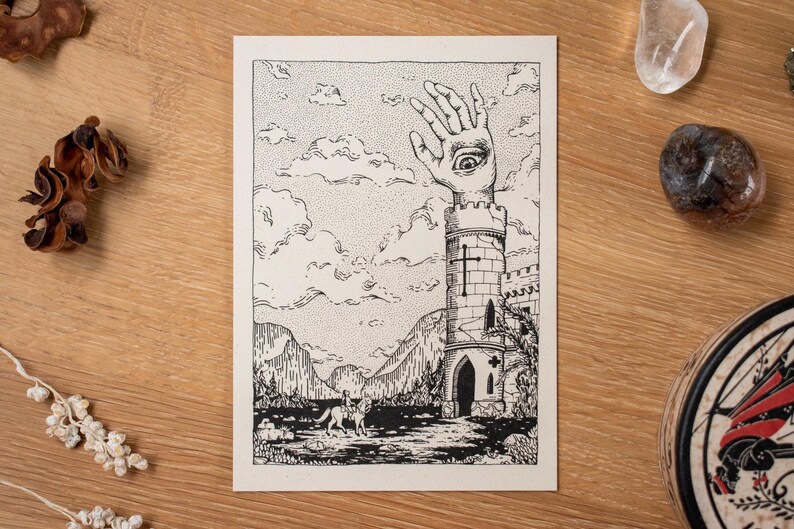 May include: Black and white illustration of a surreal landscape featuring a tower with a hand and eye, a figure on horseback, and mountains. The artwork is on a cream-colored card, with decorative elements on a wooden surface.